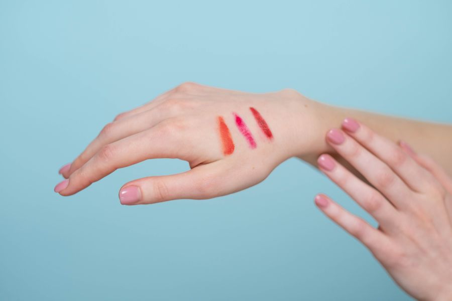 Lipstick swatches on a hand against a blue background